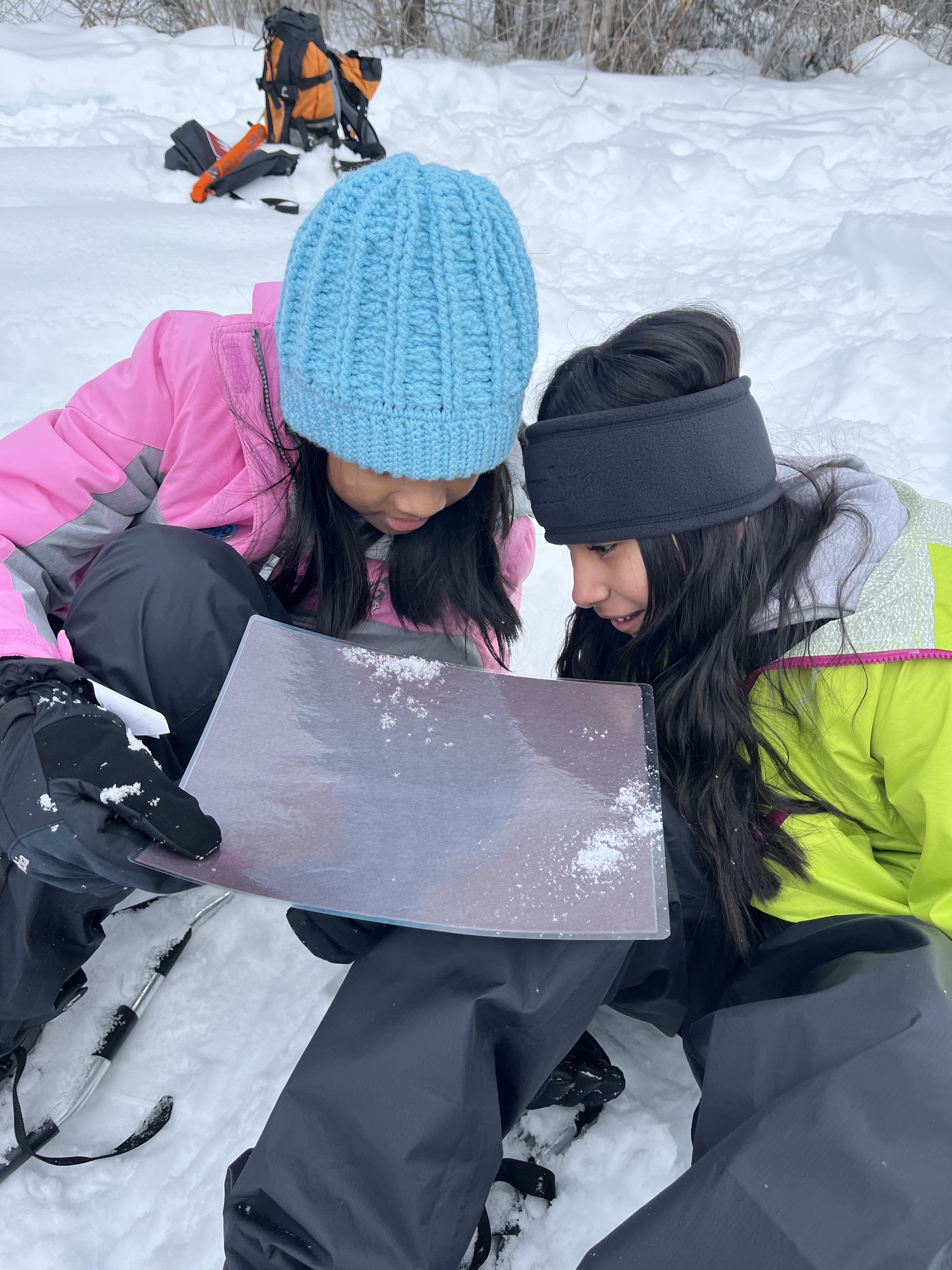 Two girls sit in the snow looking at a map together